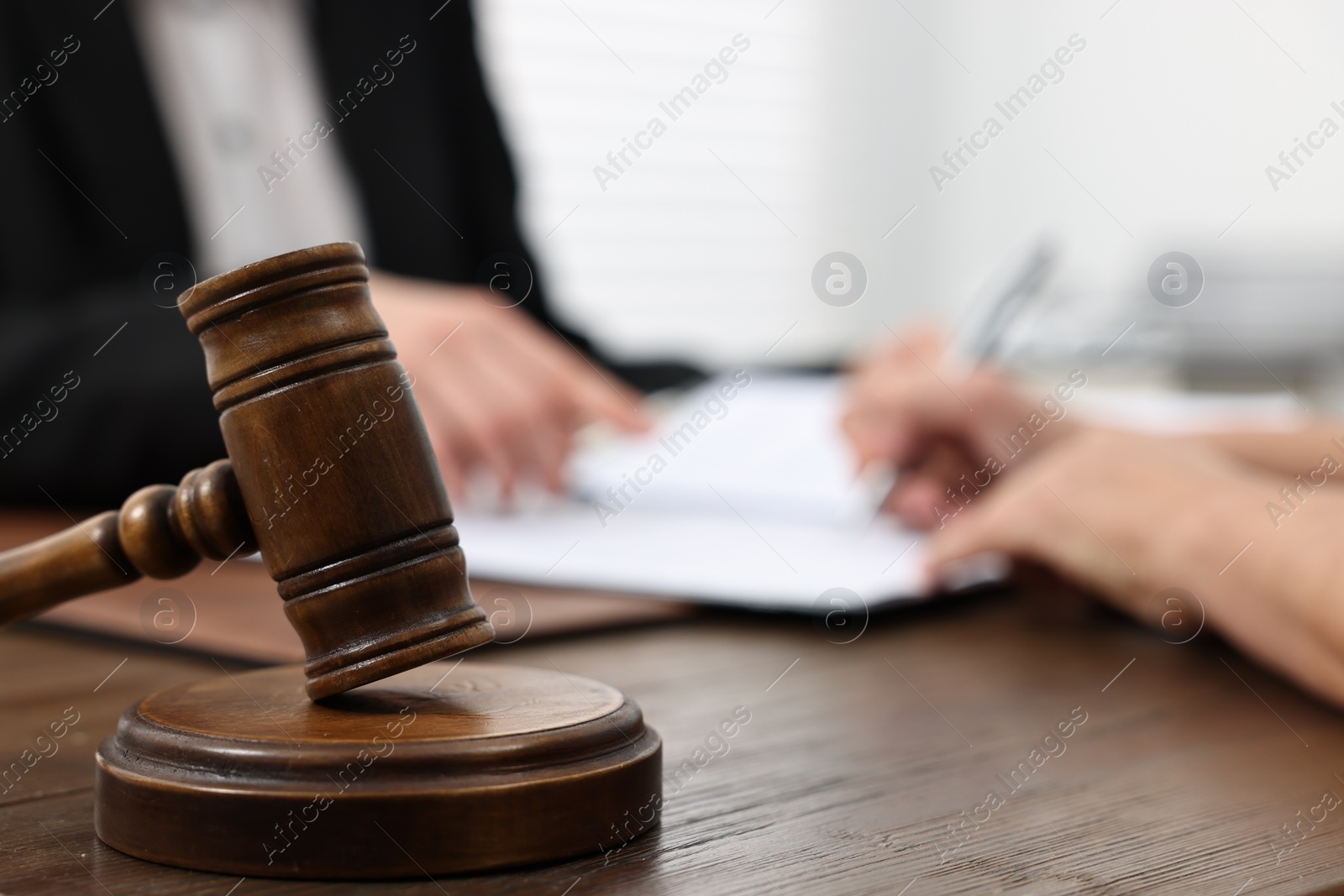 Photo of Senior woman signing document in lawyer's office, focus on gavel