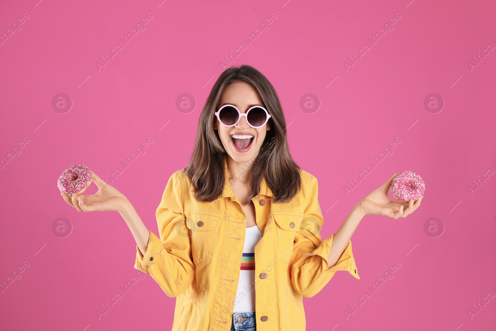 Photo of Beautiful young woman wearing sunglasses with donuts on pink background