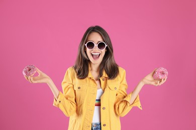 Beautiful young woman wearing sunglasses with donuts on pink background