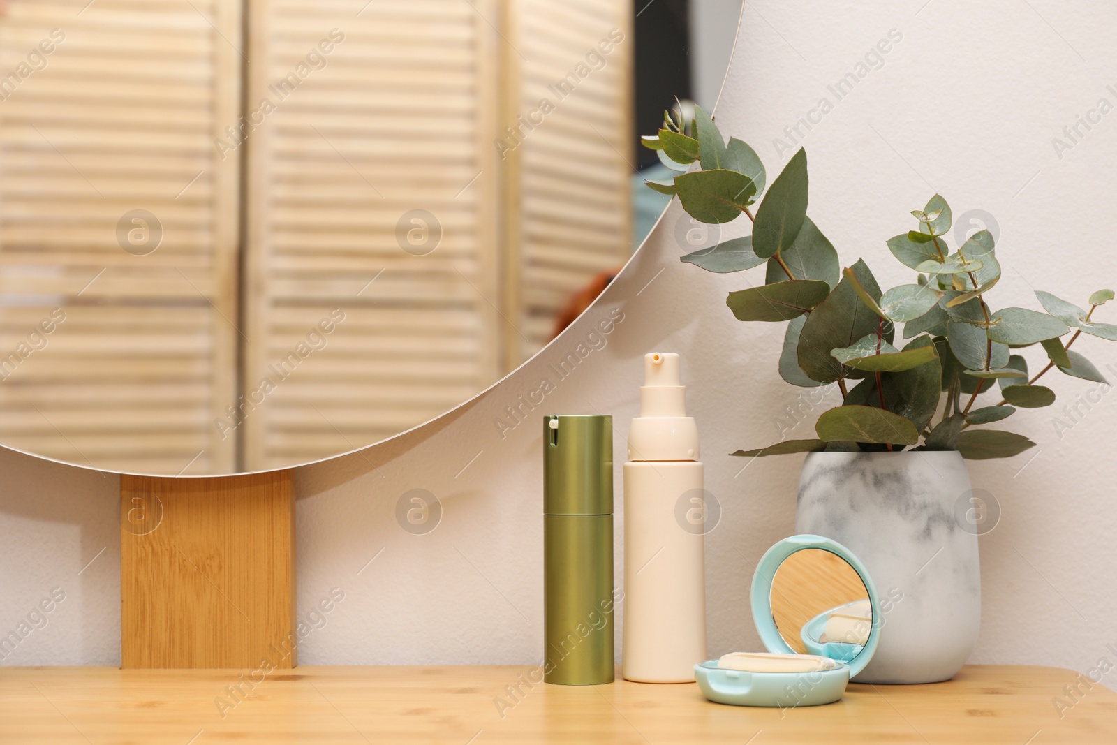 Photo of Wooden dressing table with round mirror, eucalyptus and makeup products