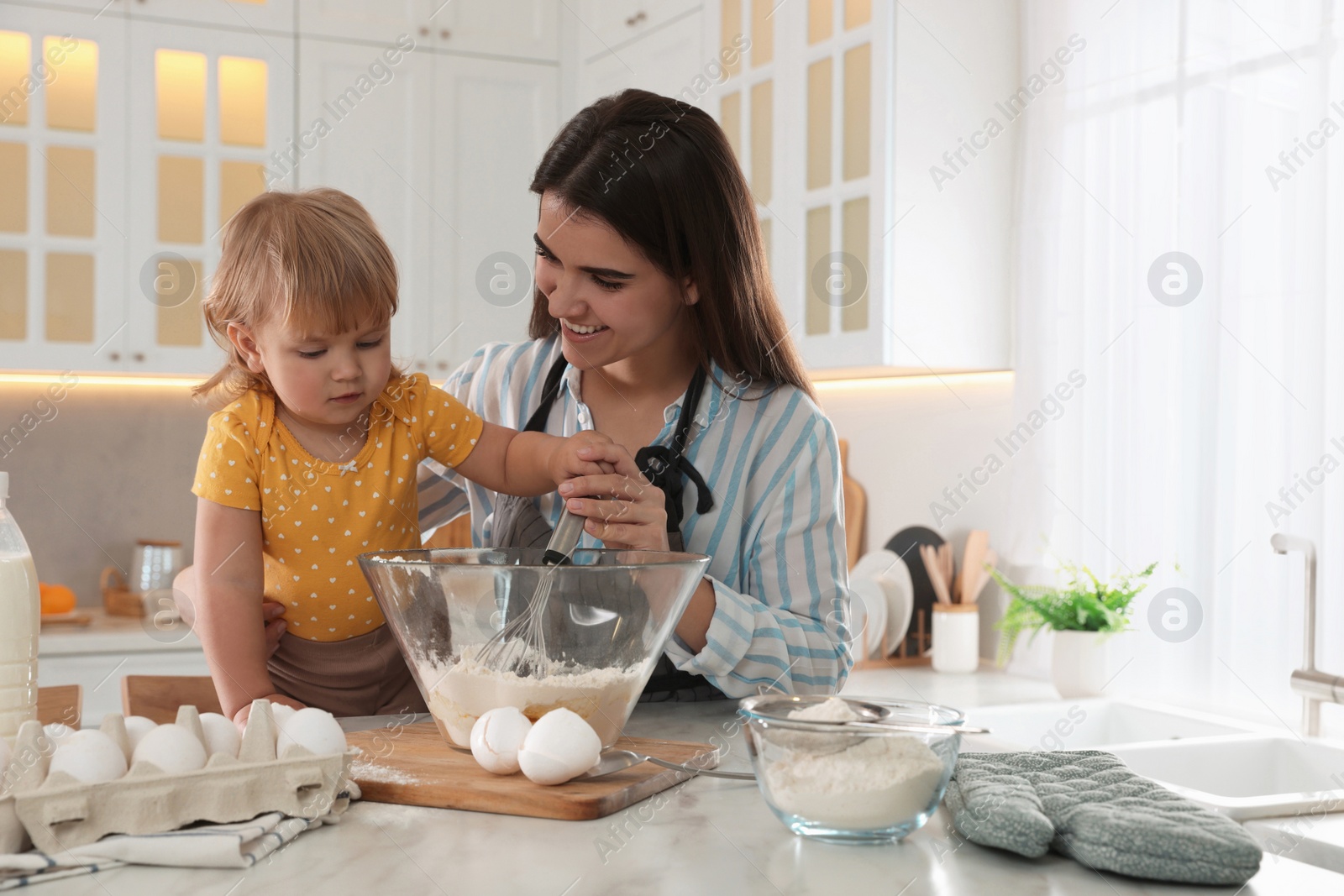 Photo of Mother and her little daughter cooking dough together in kitchen