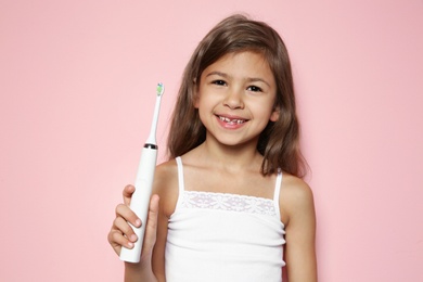 Portrait of little girl with electric toothbrush on color background