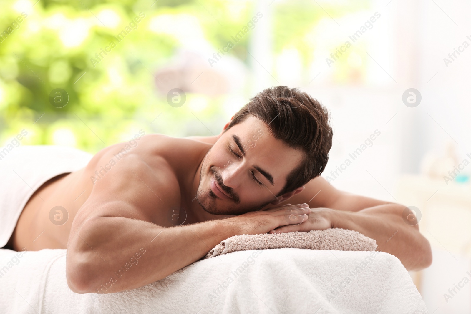 Photo of Handsome young man relaxing on massage table in spa salon