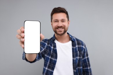 Handsome man showing smartphone in hand on light grey background, selective focus. Mockup for design