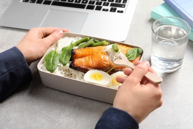 Woman eating natural protein food from container at office table