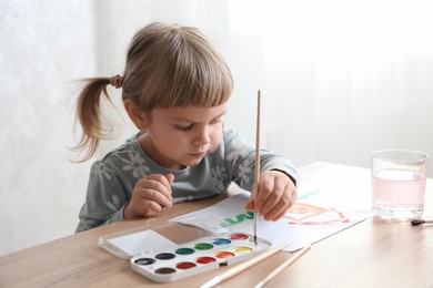 Cute little girl drawing with brush at wooden table indoors. Child`s art