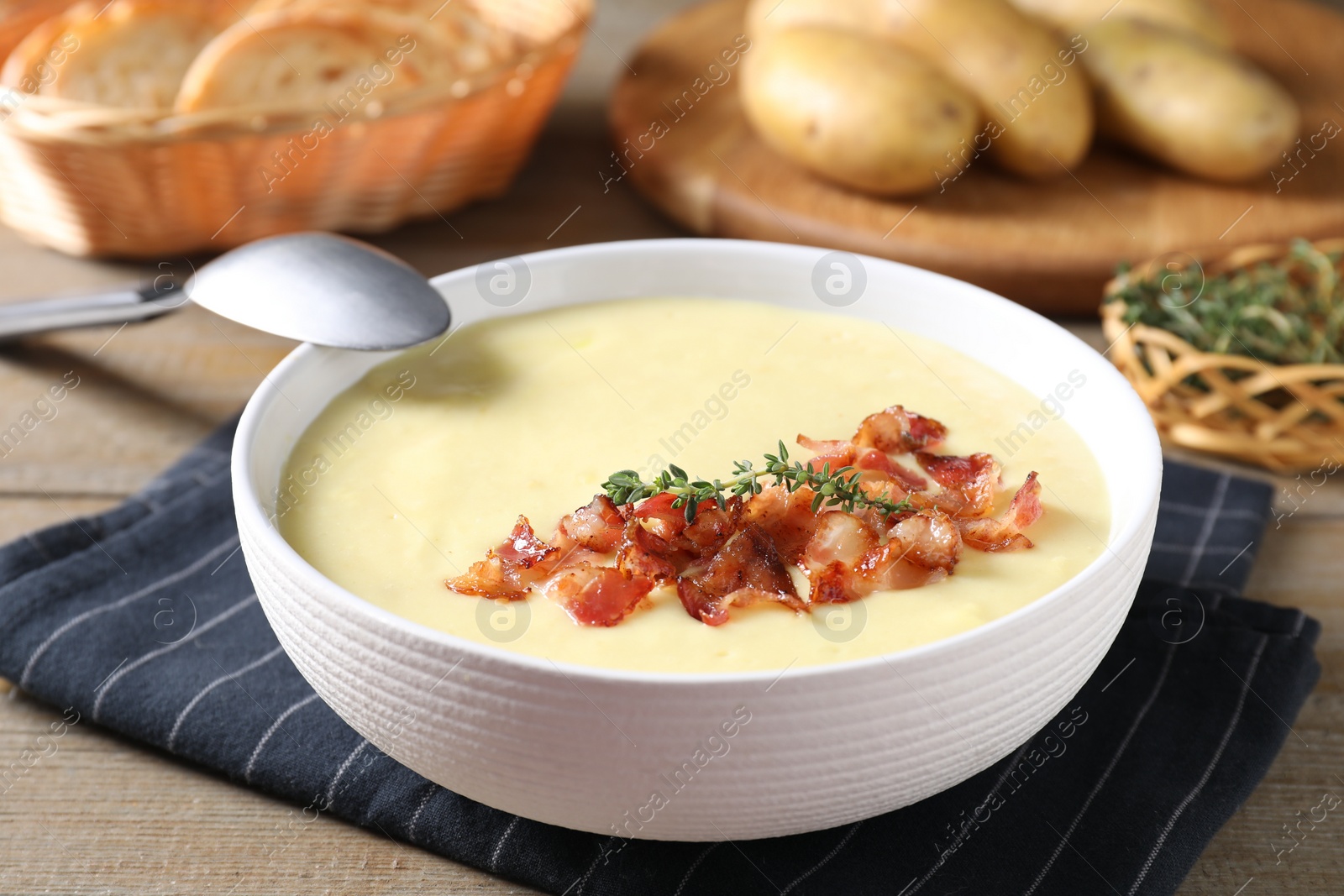 Photo of Tasty potato soup with bacon and rosemary in bowl served on wooden table