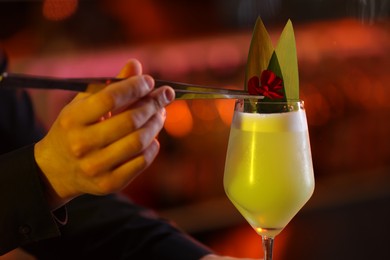 Photo of Bartender decorating fresh alcoholic cocktail with flower on blurred background
