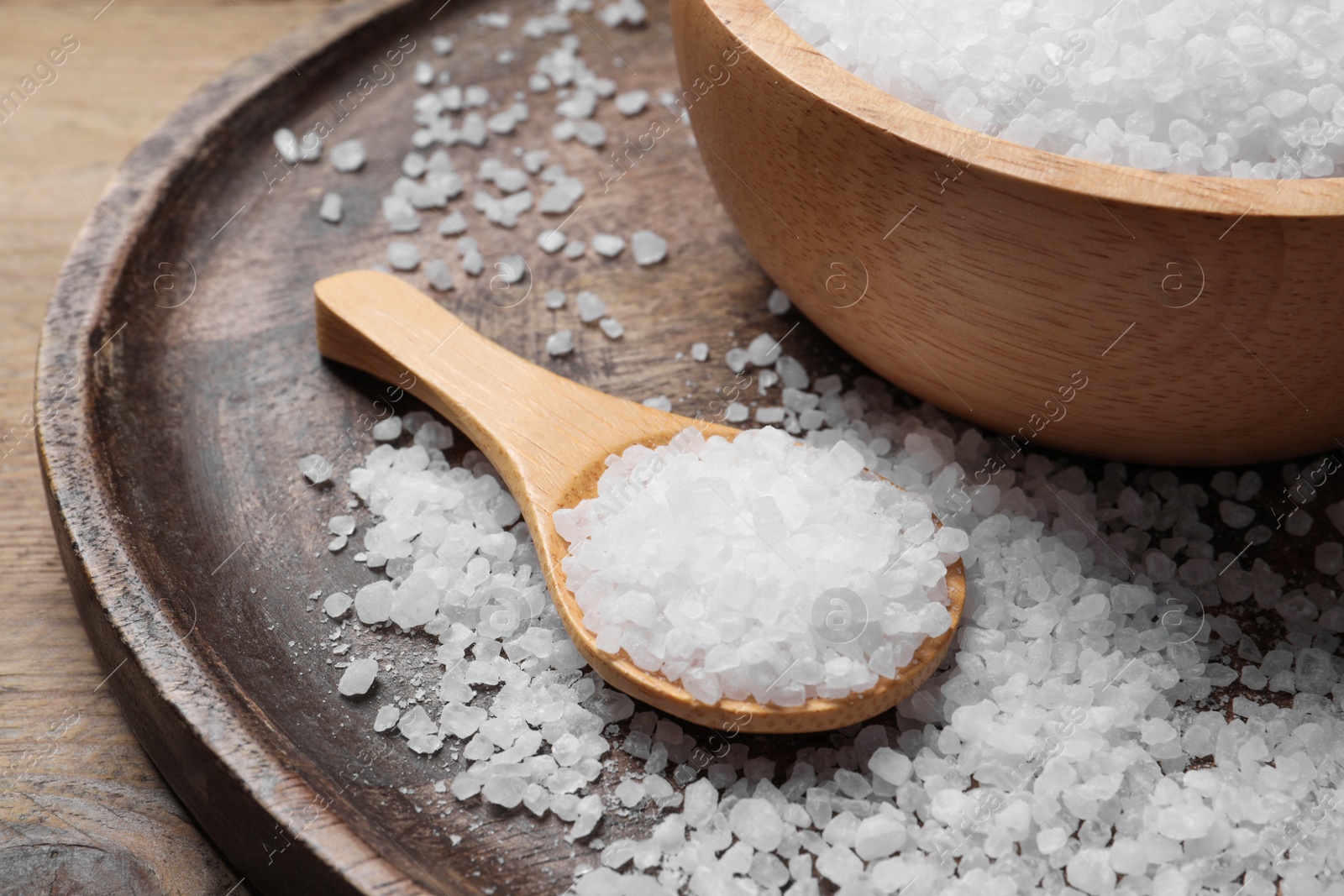 Photo of Bowl and spoon with natural sea salt on wooden table, closeup