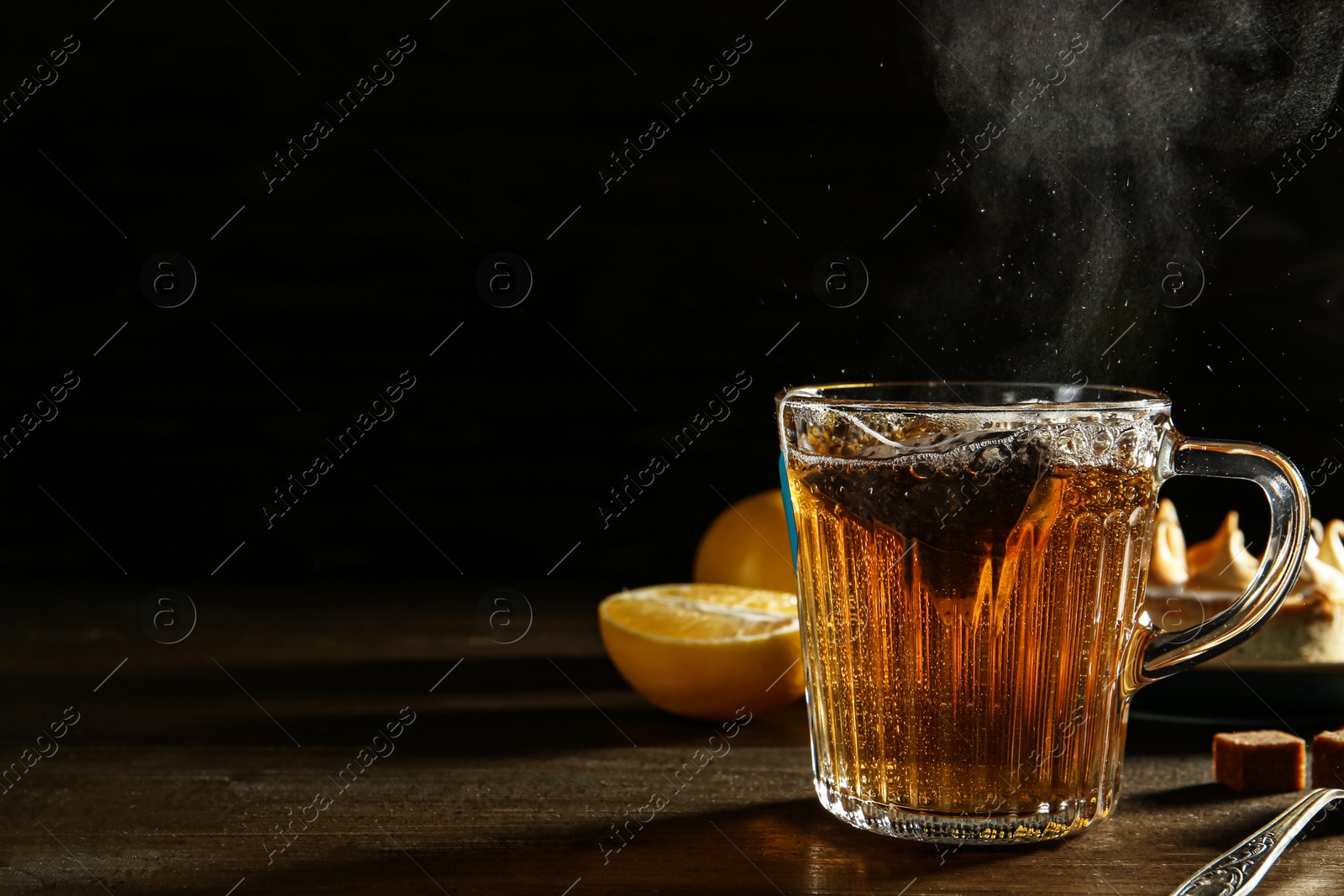 Photo of Tea bag in glass cuphot water on dark wooden table. Space for text