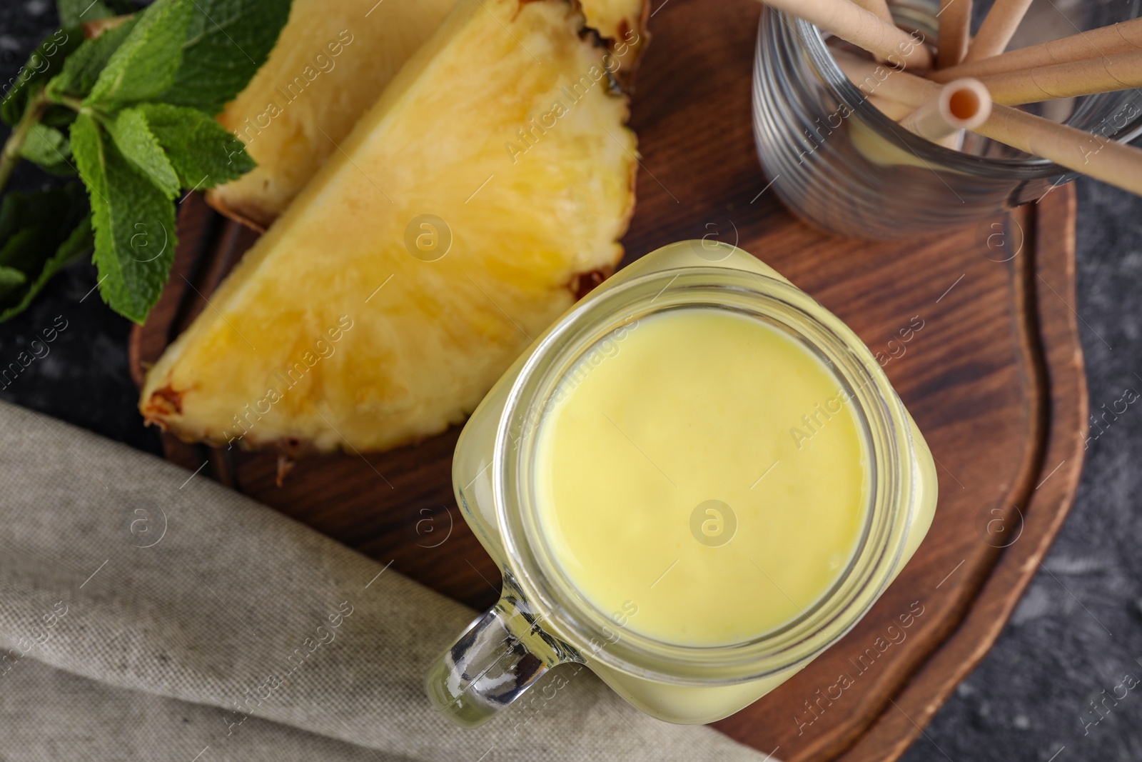 Photo of Tasty pineapple smoothie and straws on dark table, flat lay