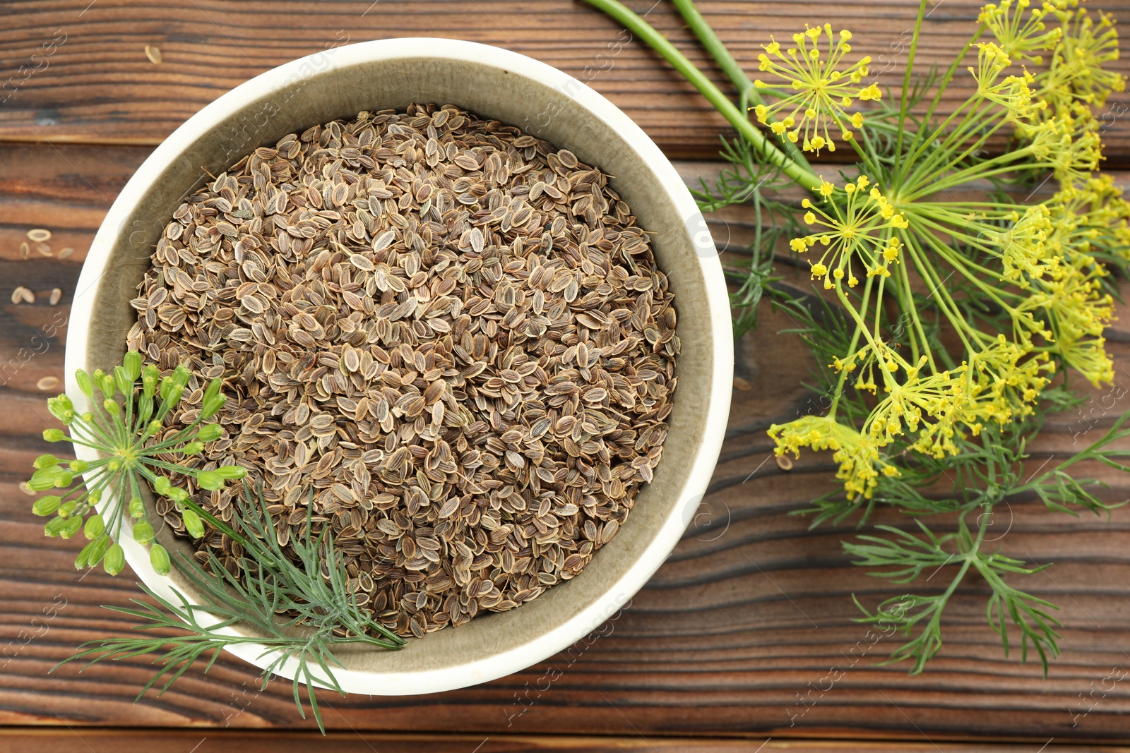 Photo of Bowl of dry seeds and fresh dill on wooden table, flat lay