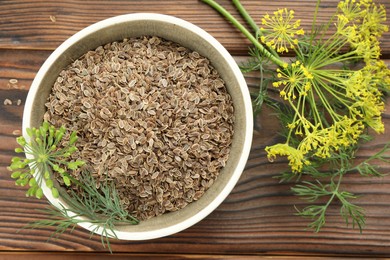 Photo of Bowl of dry seeds and fresh dill on wooden table, flat lay