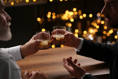 Men with glasses of whiskey talking at wooden table in bar