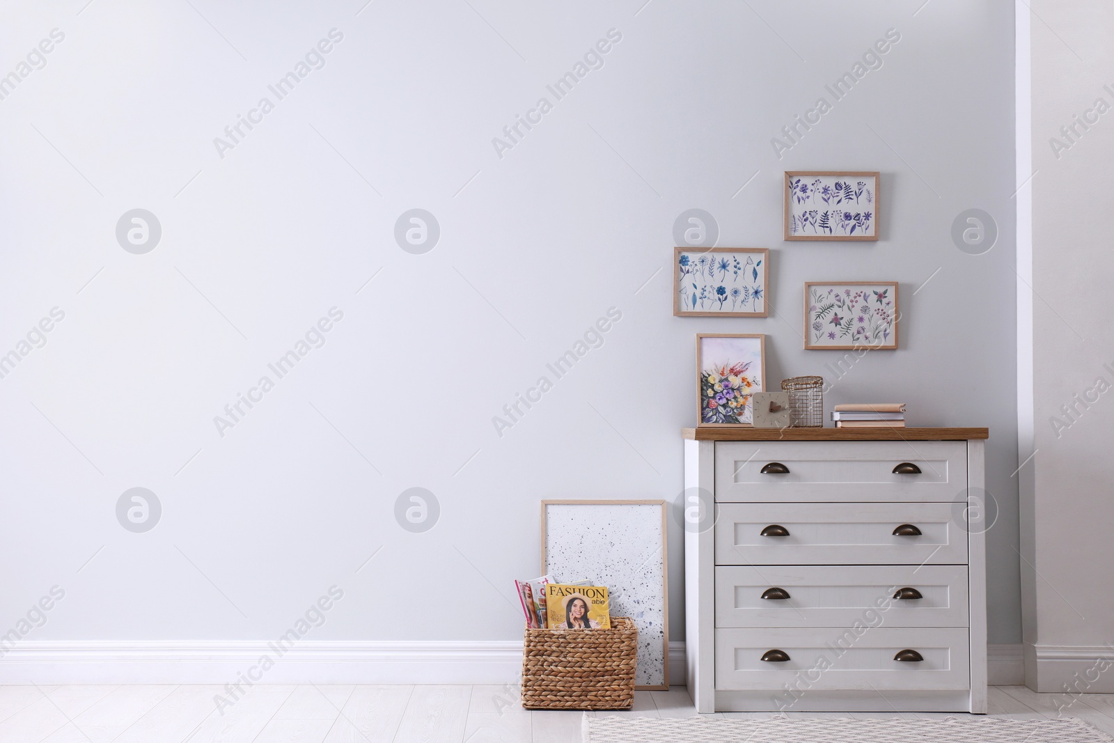 Photo of Wooden chest of drawers with books and decor near white wall in room, space for text. Interior design