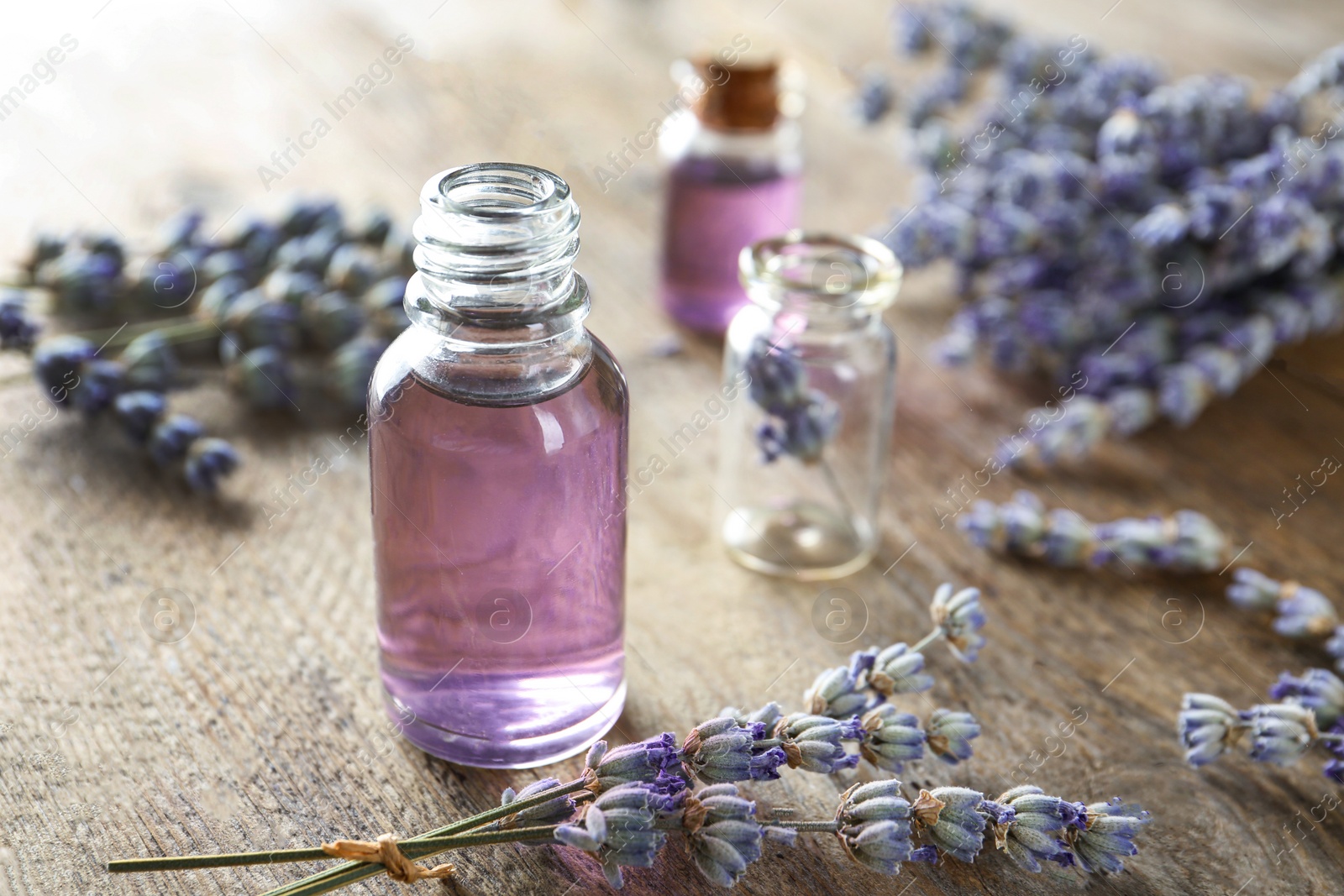 Photo of Bottle of natural essential oil and lavender flowers on wooden background