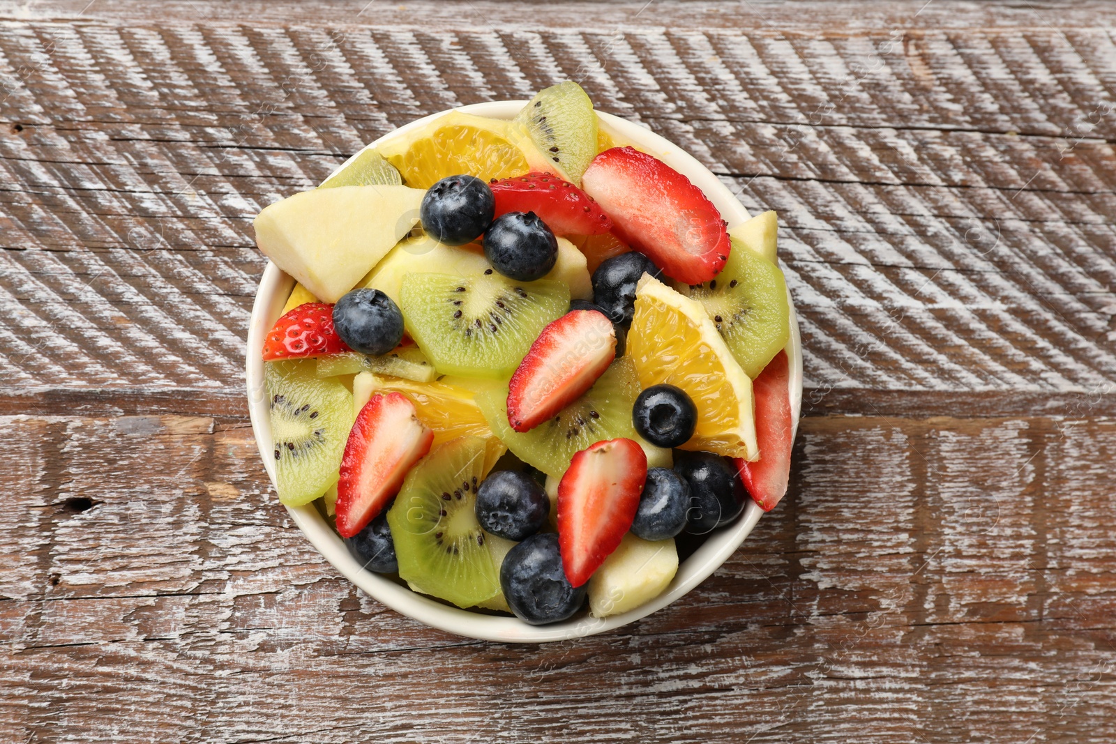 Photo of Tasty fruit salad in bowl on wooden table, top view