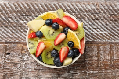 Photo of Tasty fruit salad in bowl on wooden table, top view