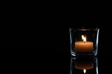 Wax candle in glass burning on dark background