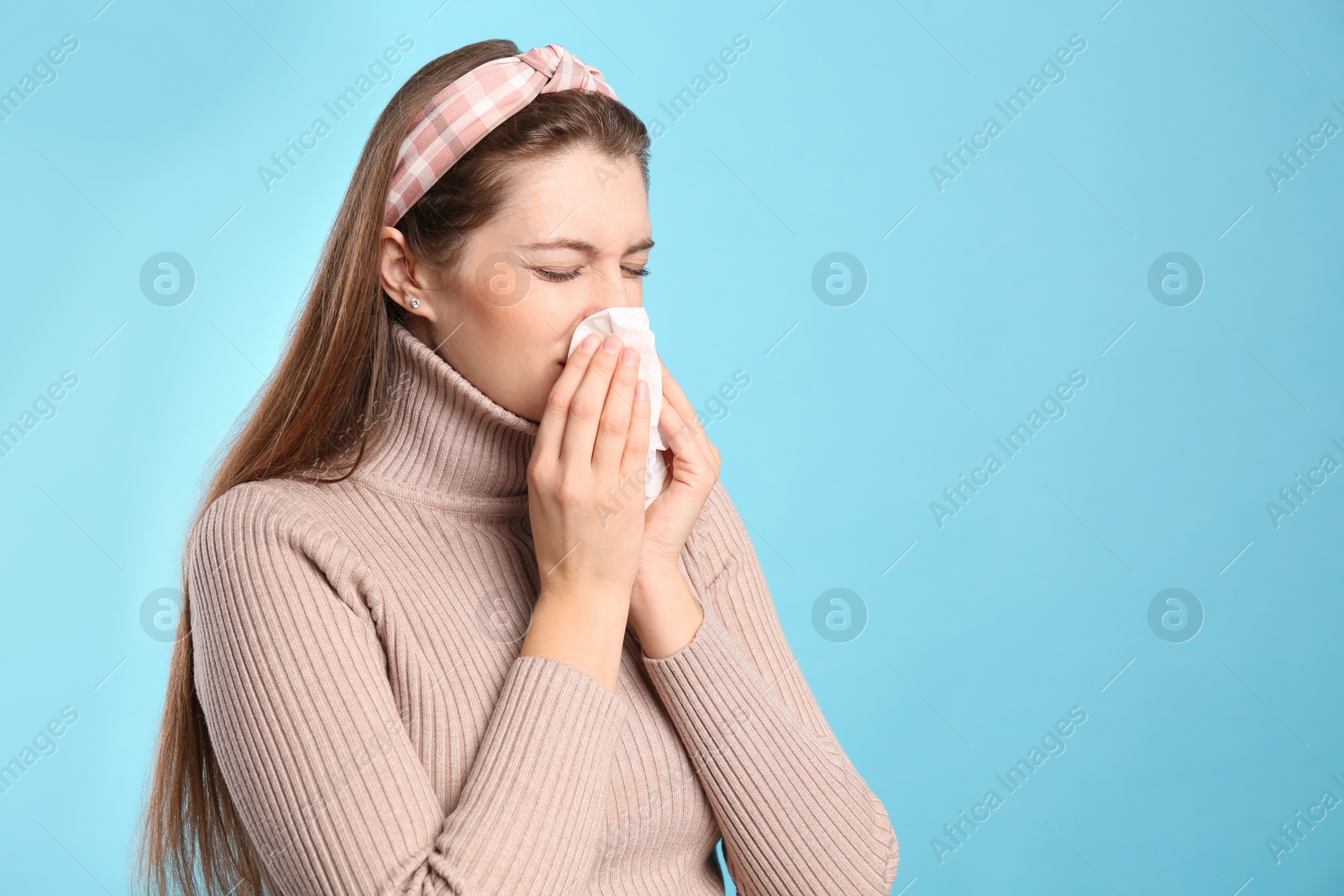 Photo of Young woman with tissue suffering from runny nose on light blue background. Space for text