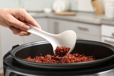 Photo of Woman taking brown rice from multi cooker with spoon in kitchen, closeup