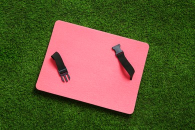 Photo of Pink foam seat mat for tourist on green grass, top view