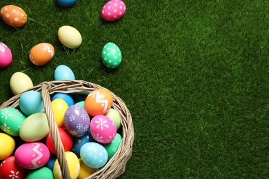 Photo of Colorful Easter eggs in basket on green grass, above view. Space for text