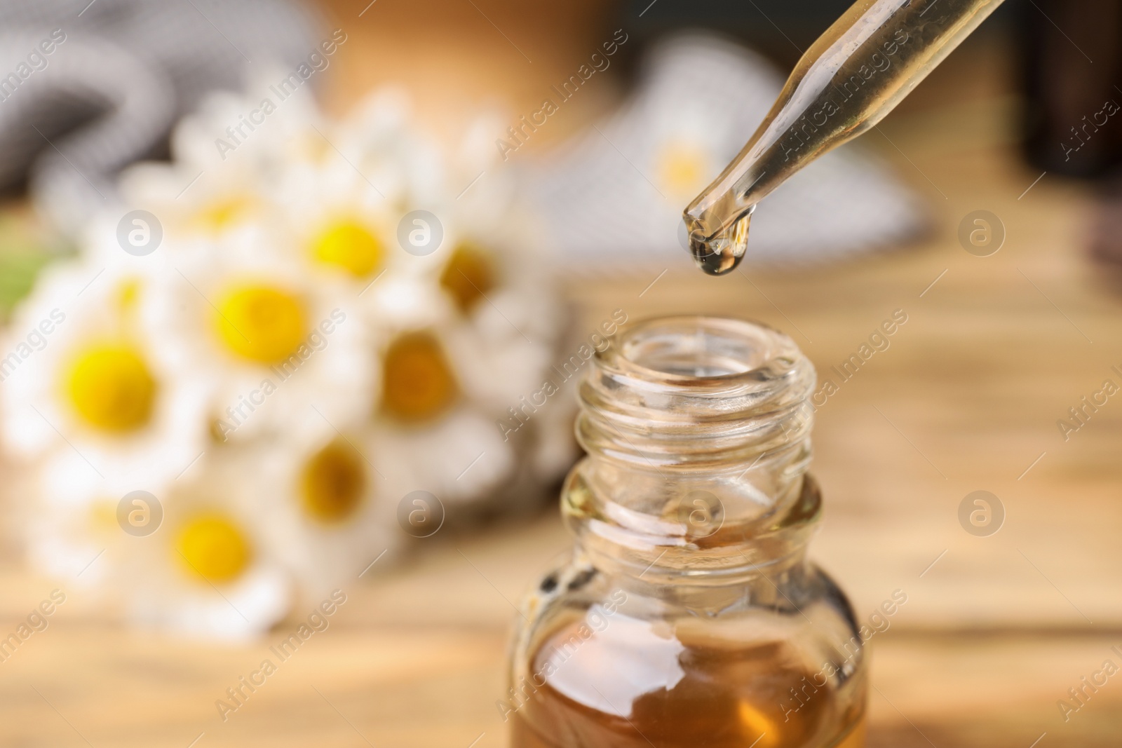 Photo of Pipette with essential oil over bottle on blurred background, closeup. Space for text