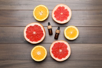 Photo of Bottles of citrus essential oils and fresh fruits on wooden table, flat lay