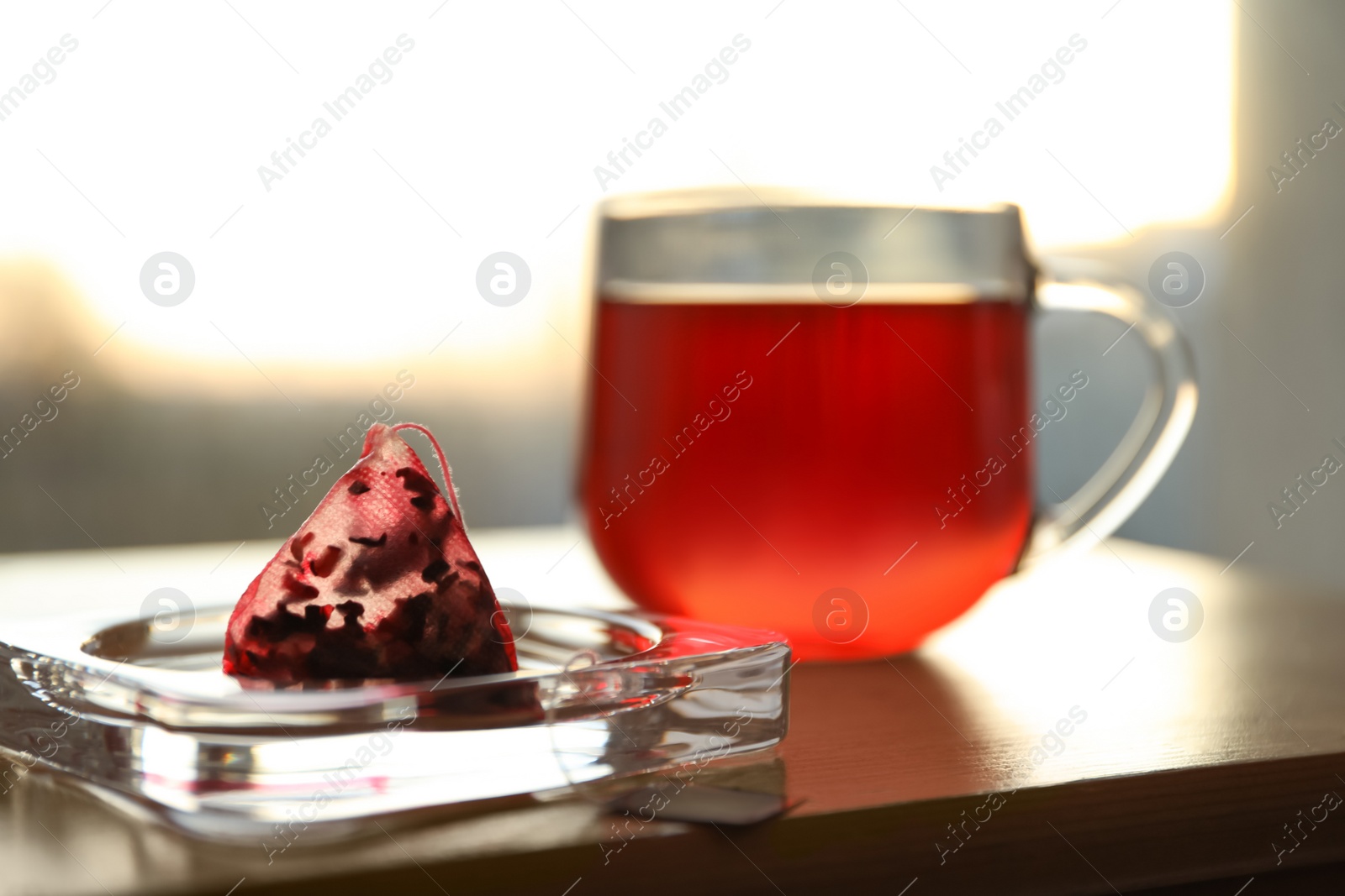 Photo of Saucer with used pyramid tea bag on table. Space for text