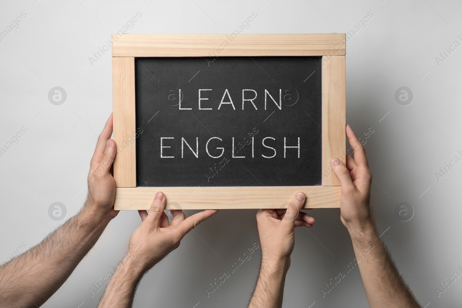 Image of Men holding chalkboard with text Learn English on light background, closeup