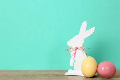 Cute wooden Easter bunny and dyed eggs on table against color background, space for text