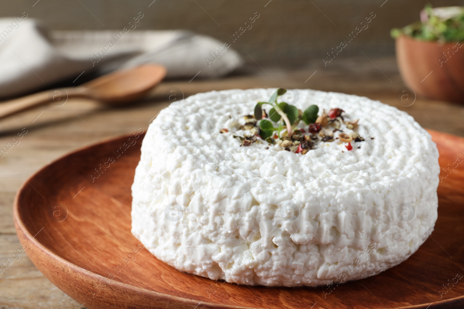 Photo of Wooden plate of fresh cottage cheese with spice and microgreens on table, closeup