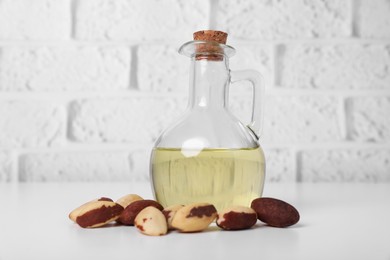 Tasty Brazil nuts and bottle with oil on white table against brick wall