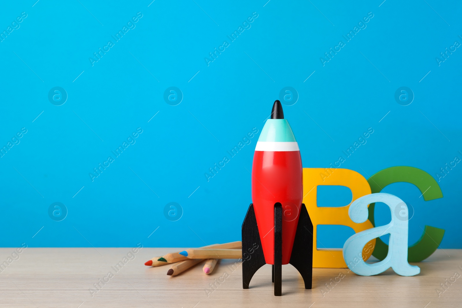 Photo of Bright toy rocket and school supplies on wooden desk. Space for text