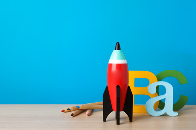 Bright toy rocket and school supplies on wooden desk. Space for text