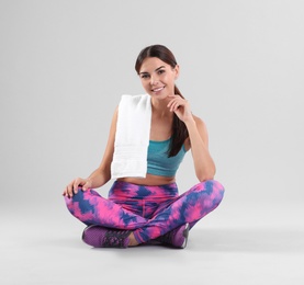 Photo of Beautiful young woman in sportswear with towel sitting on white background