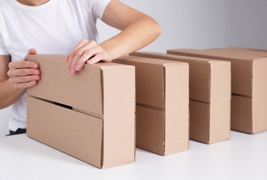 Photo of Woman folding cardboard boxes at white table, closeup. Production line