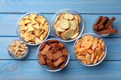 Photo of Different crispy rusks in bowls on light blue wooden table, flat lay