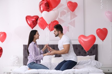 Romantic couple with heart shaped balloons in bedroom. Valentine's day celebration