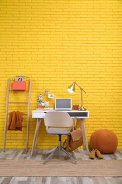 Stylish home office interior with comfortable workplace near yellow brick wall