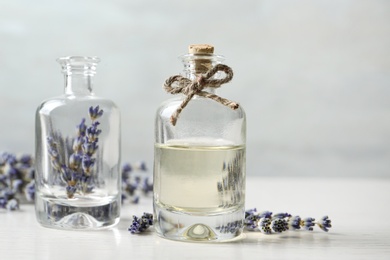 Photo of Bottles with natural essential oil and lavender flowers on white wooden table