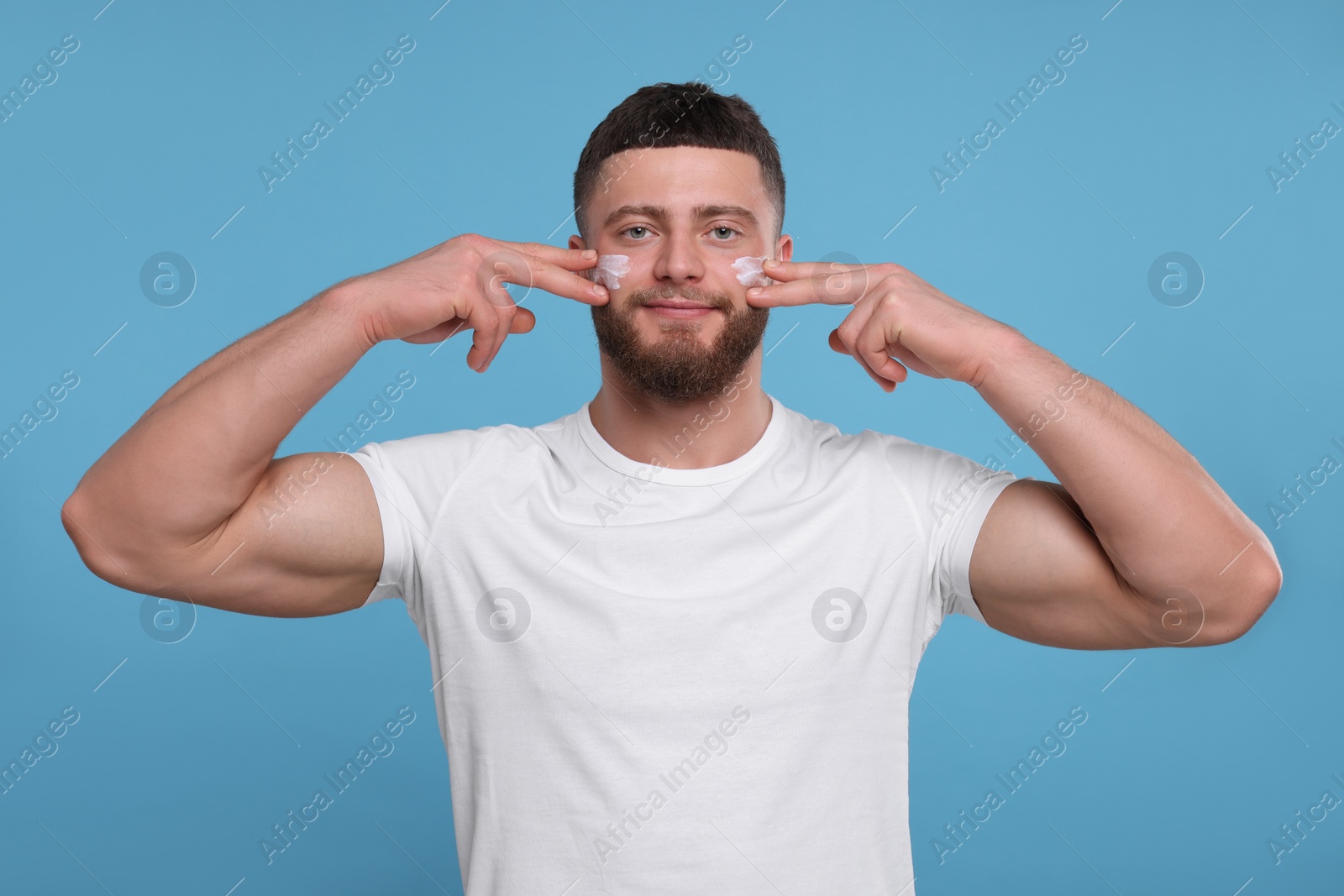 Photo of Handsome man applying cream onto his face on light blue background