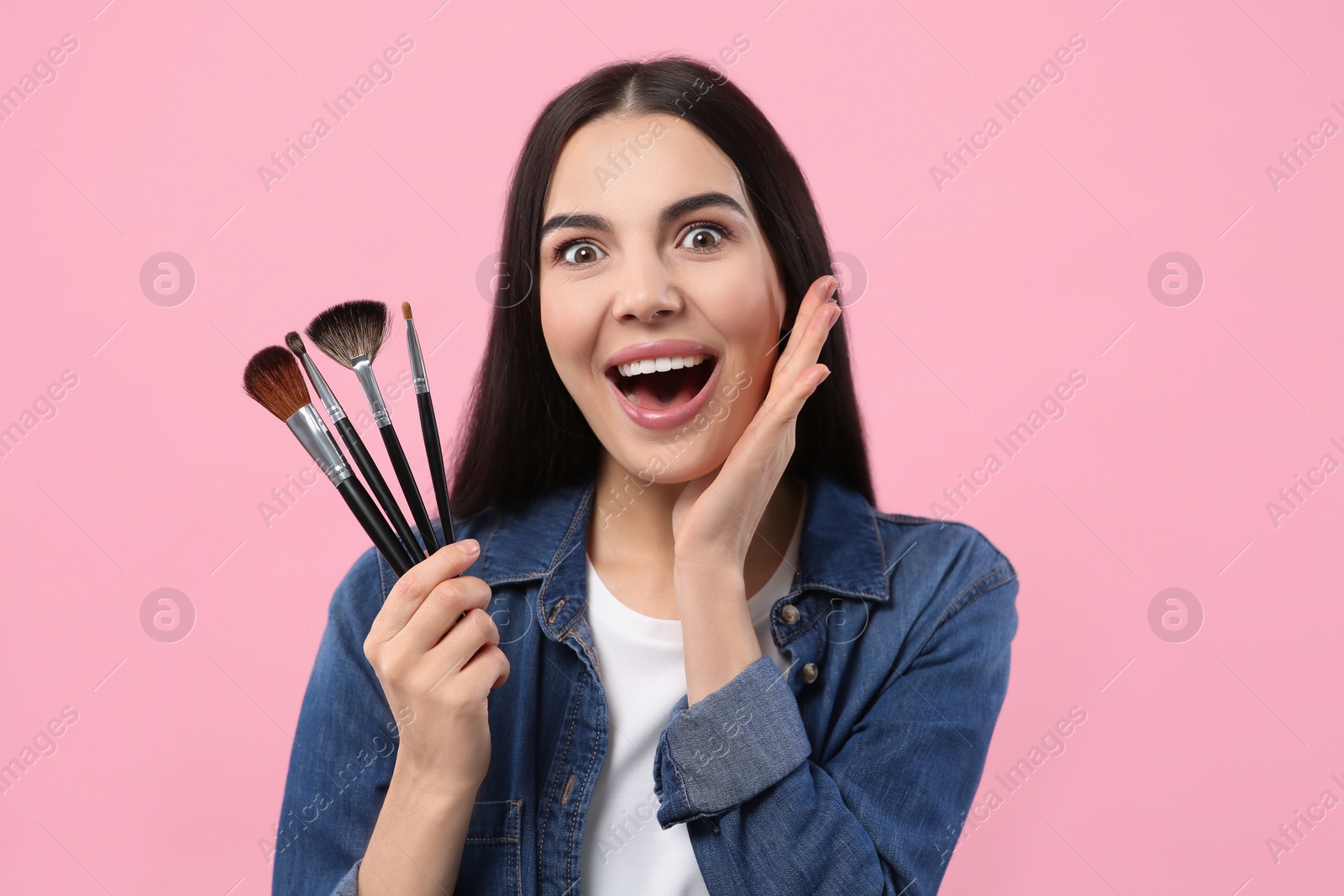 Photo of Happy woman with different makeup brushes on pink background