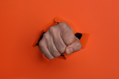 Photo of Man breaking through orange paper with fist, closeup
