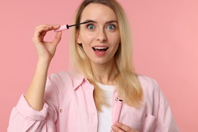 Photo of Beautiful woman applying mascara on pink background