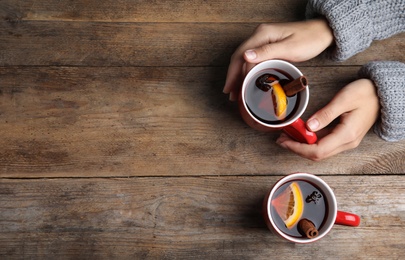 Photo of Woman with cups of hot winter drink at wooden table, top view. Space for text