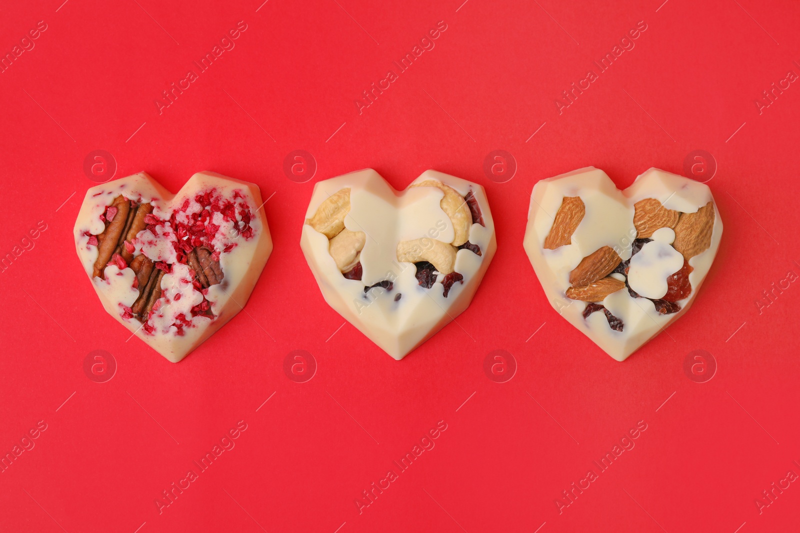 Photo of Tasty chocolate heart shaped candies with nuts on red background, flat lay