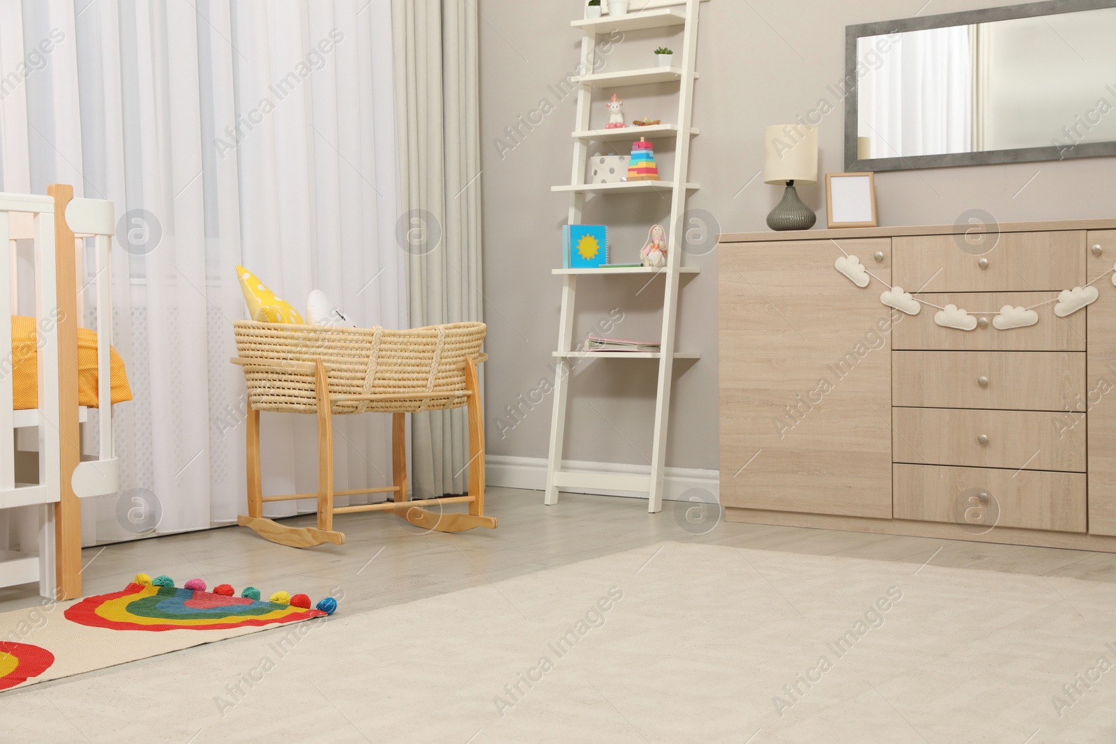 Photo of Beautiful cradle with toys near crib and dresser in baby room. Interior design