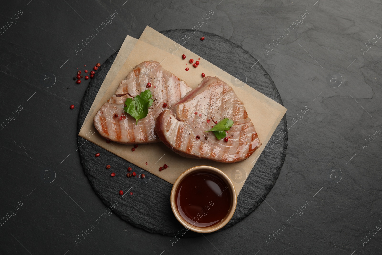 Photo of Delicious tuna steaks with sauce, parsley and spices on black table, top view